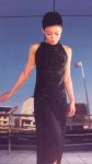 [Vanessa in long black body-skimming sleeveless dress, by road, buildings opposite]